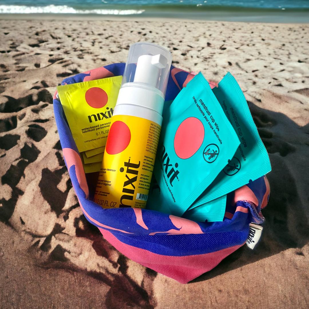 the nixit travel pouch sits open on sand, with the nixit menstrual cup wipes, nixit travel wash and nixit lubricant sachets on display inside the pouch